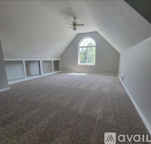 A spacious attic room with a ceiling fan and a large window.