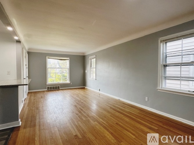 A spacious room with wooden floors and two windows.