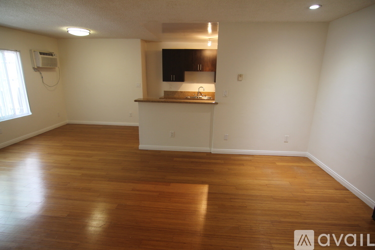 A room with wooden floors and a kitchenette in the corner.