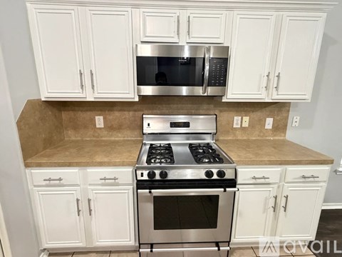 A kitchen with white cabinets and a stainless steel stove and microwave.