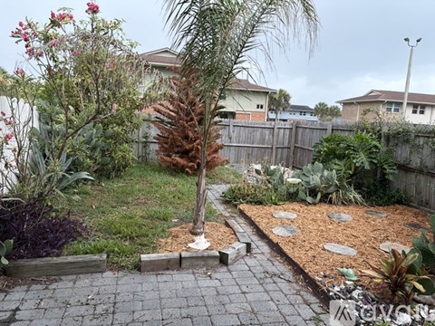 A backyard with a tree, a fence, and a brick walkway.