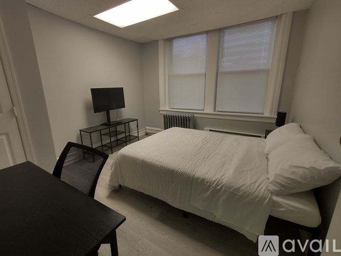 A bedroom with a bed, chair, and a small table with a monitor on it.