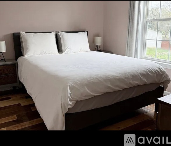 A bed with white bedding sits in a room with wooden floors and a window.