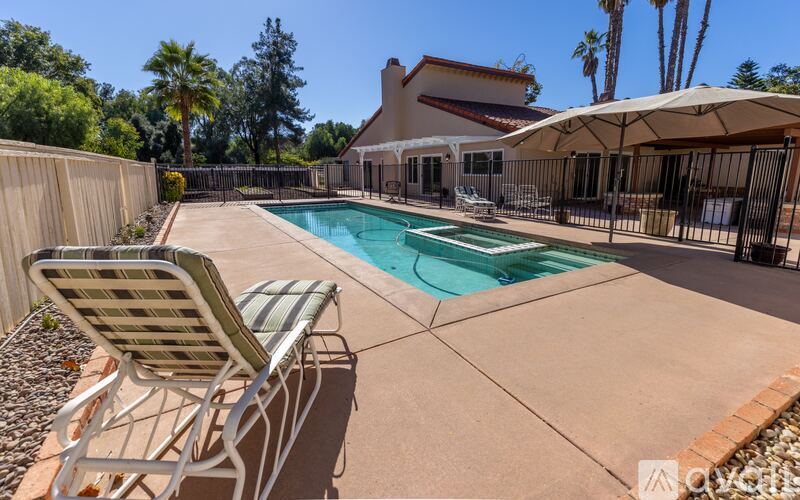 A pool with a chair and umbrella in front of a house.