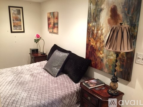 A bedroom with a bed, a nightstand with a lamp, a painting, and a framed picture on the wall.