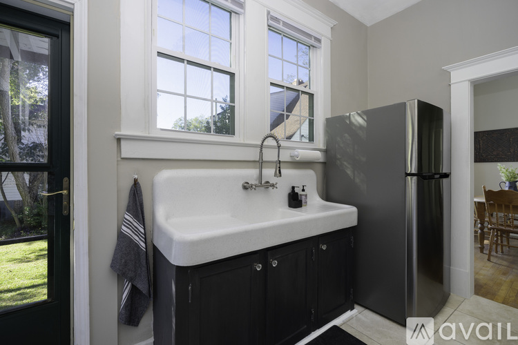 A bathroom with a sink, window, and a black refrigerator.