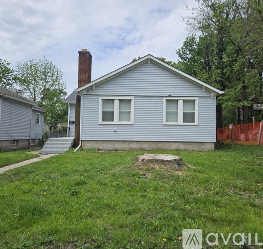 A small house with a grey siding and a white window is surrounded by a grassy area.
