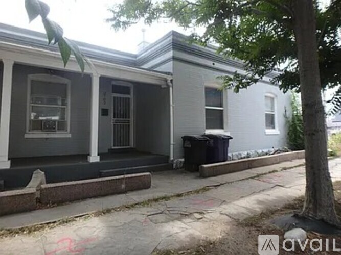A grey house with a black trash bin in front.