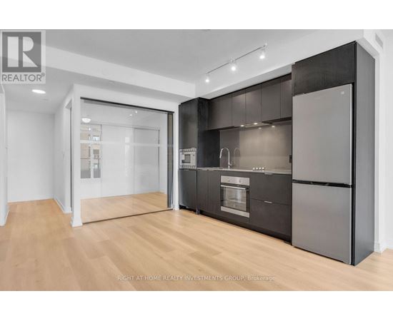 A modern kitchen with dark cabinets and a wooden floor.