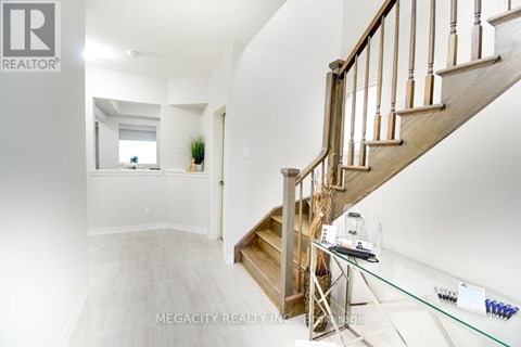 A spacious hallway with a wooden staircase and a glass table with a few items on it.