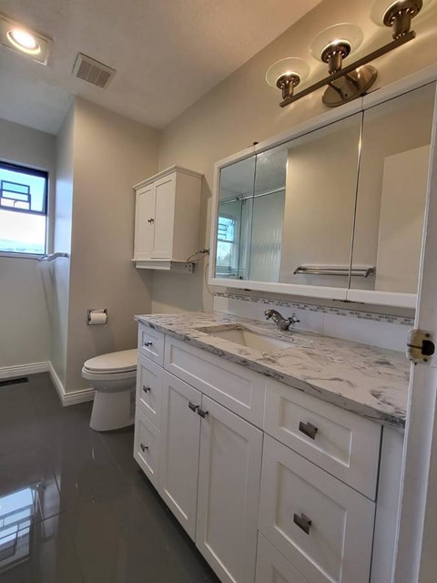 A white bathroom with a marble counter top and a large mirror.