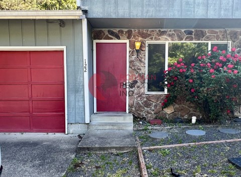A red door is on the left side of a grey building.