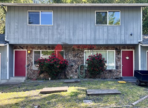 A house with a red door and windows with red flowers in front.