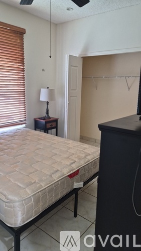A bedroom with a bed, a nightstand with a lamp, and a black dresser.