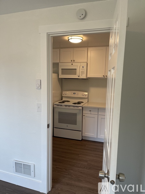A kitchen with white cabinets and appliances is visible through an open door.