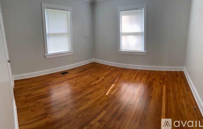 A room with wooden flooring and two windows.