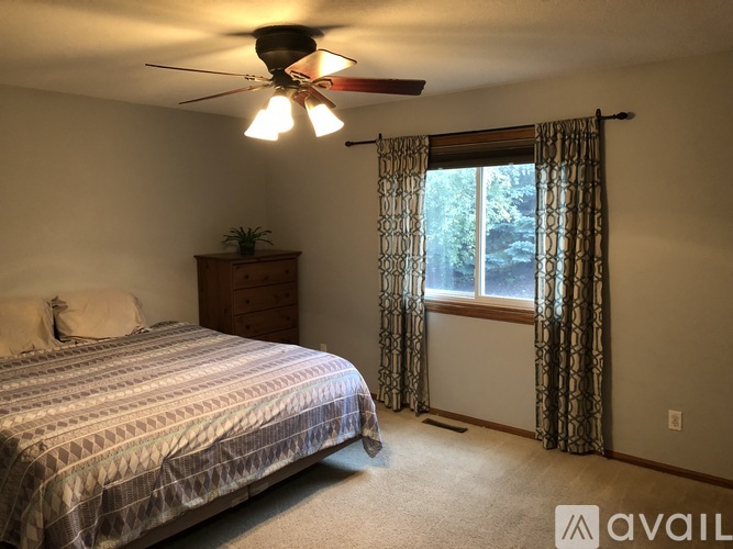 A bedroom with a bed, dresser, and window with curtains.