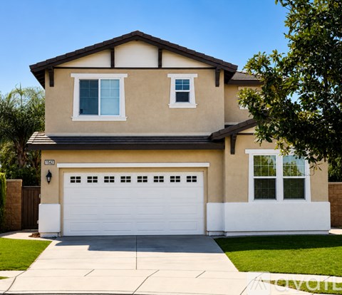 A beige house with a white garage door and a brown roof.
