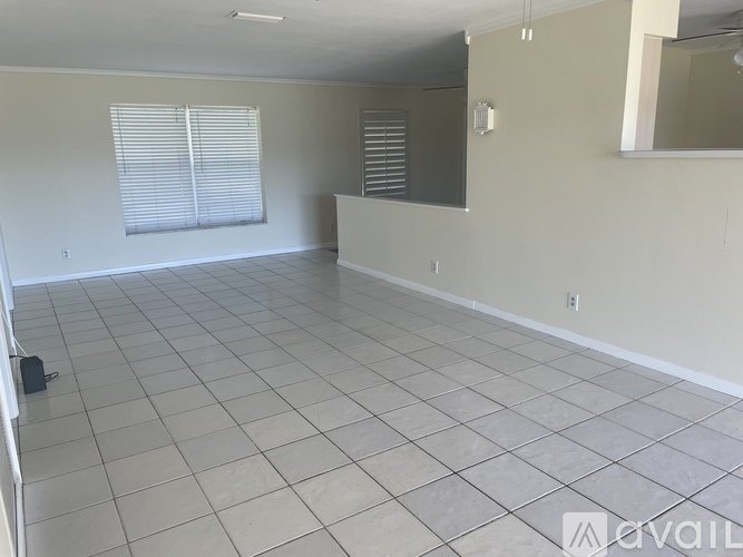 A spacious room with tiled flooring and a large window with blinds.