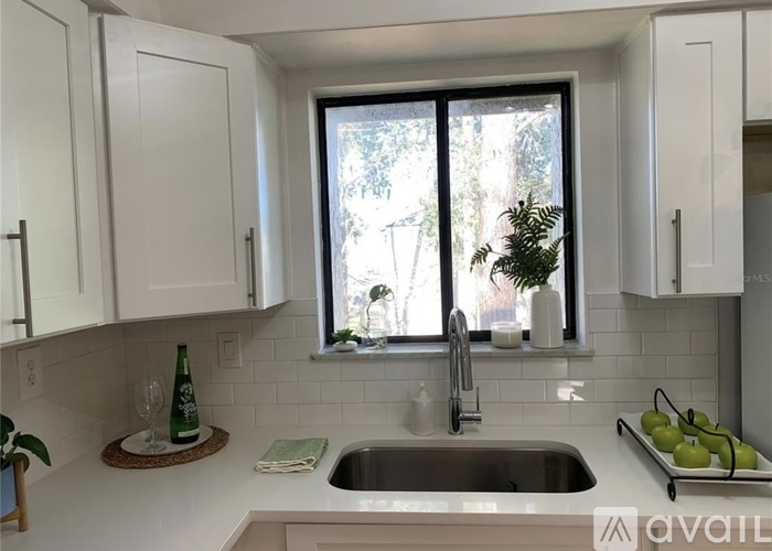 A kitchen with white cabinets and a window overlooking a tree.