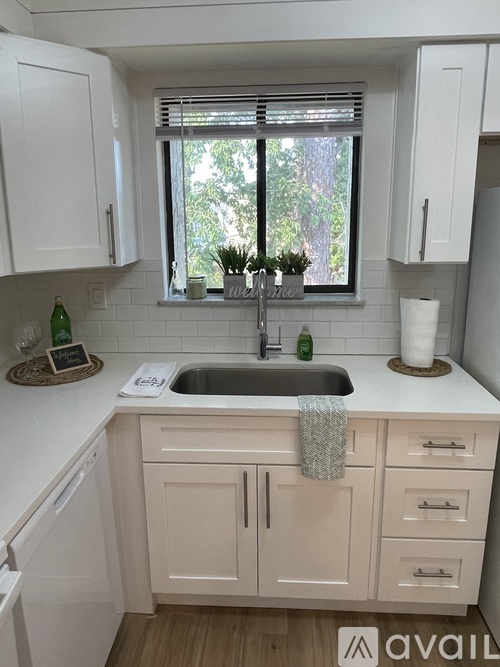 A kitchen with white cabinets and a window with blinds.
