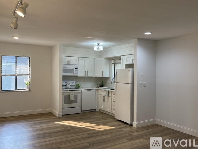 A well-lit, spacious kitchen with white appliances and wooden flooring.