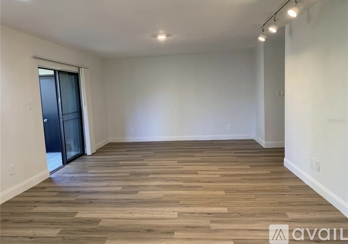 A spacious room with wooden flooring and a sliding glass door.
