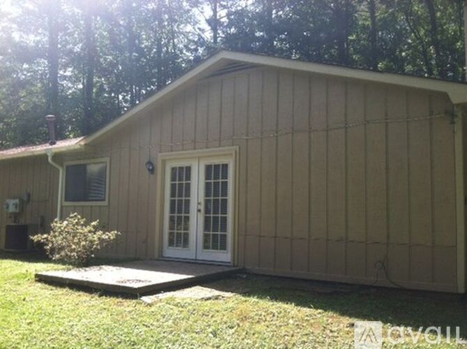 A small house with a white door and a window is surrounded by trees.