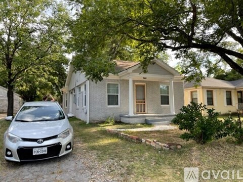 A white car is parked in front of a house with a tree in the front yard.