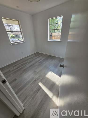 A room with wooden flooring and two windows.