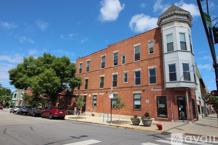 A street view of a red brick building with a white tower on the corner.