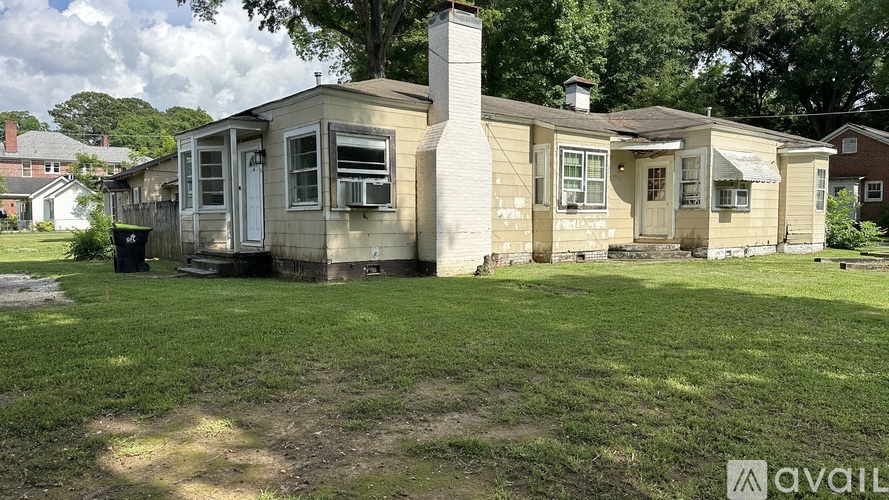 A house with a beige siding and a brown roof is surrounded by a grassy area.