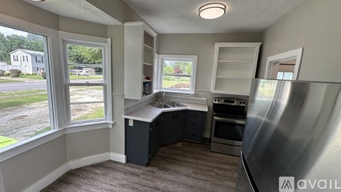 A kitchen area with a stainless steel refrigerator, a window with a view of a street, and a countertop with cabinets.