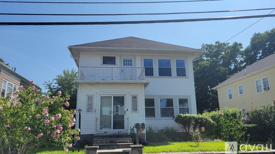 A white house with a brown roof and a balcony on the second floor.