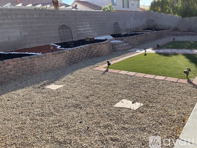 A backyard with a gravel area and a grassy area with a wall and a fence.