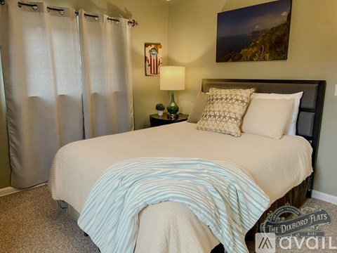 A bedroom with a bed, a nightstand with a lamp, and a painting on the wall.