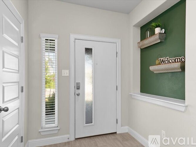 A white door with a glass panel is in a room with a green wall and a shelf with a "Welcome" sign.