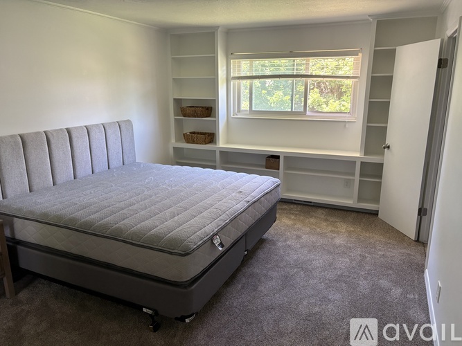 A bedroom with a bed, shelves, and a window.