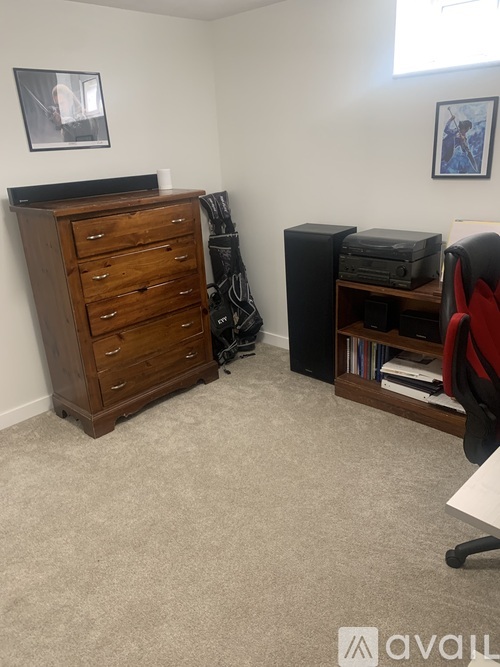 A room with a wooden chest of drawers, a black speaker, a red chair, and a small desk with a laptop on it.