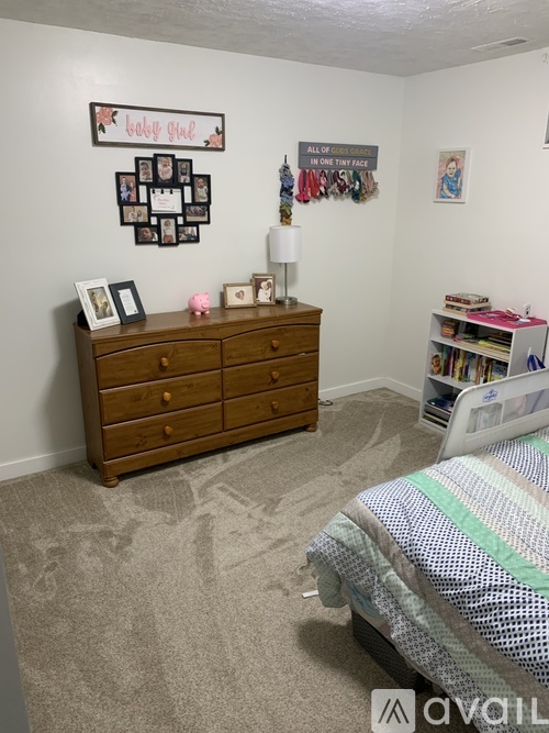 A bedroom with a bed, dresser, and a wall hanging that says "take you".