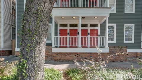 A tree grows next to a house with a red door.