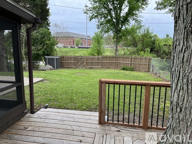 A wooden deck with a railing overlooks a grassy yard.