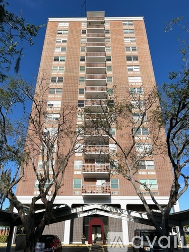 A tall brick building with balconies and trees in front.