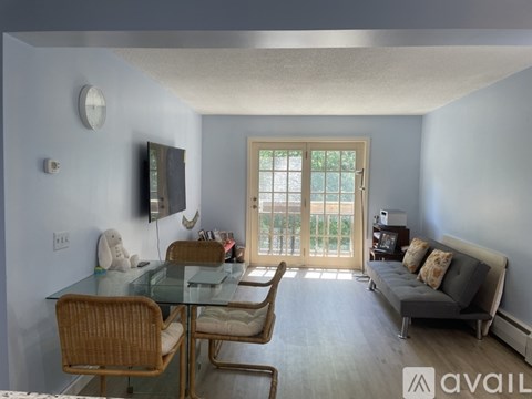A living room with a glass table and chairs, a grey sofa, and a television.