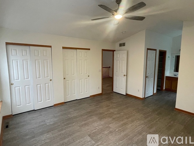 A spacious room with a ceiling fan and three doors.