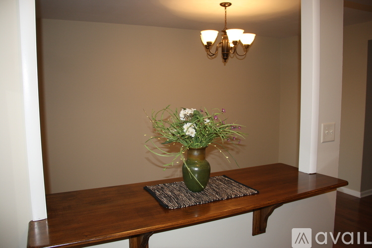 A green vase with flowers sits on a placemat on a wooden table.