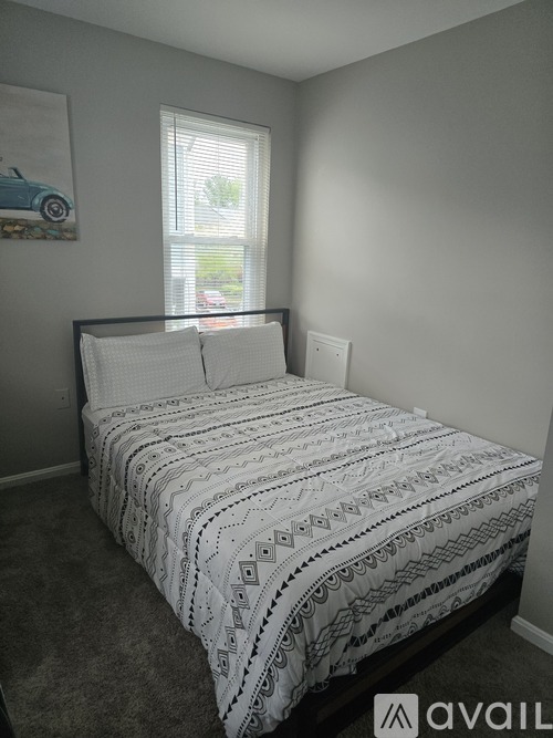 A bed with a white comforter in a room with a window.