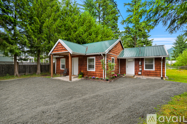 A house with a green roof is surrounded by trees and has a gravel driveway.