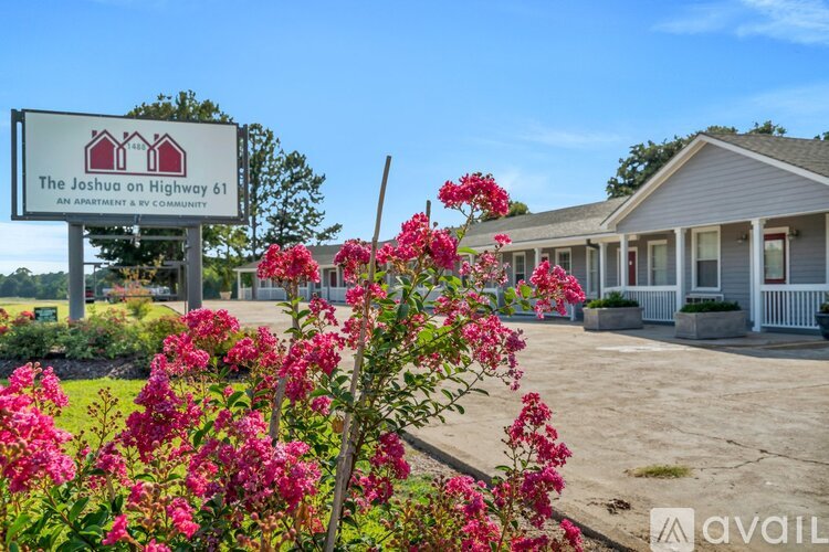 A sign for The Joshua on Highway 61 is in front of a building with flowers in the foreground.