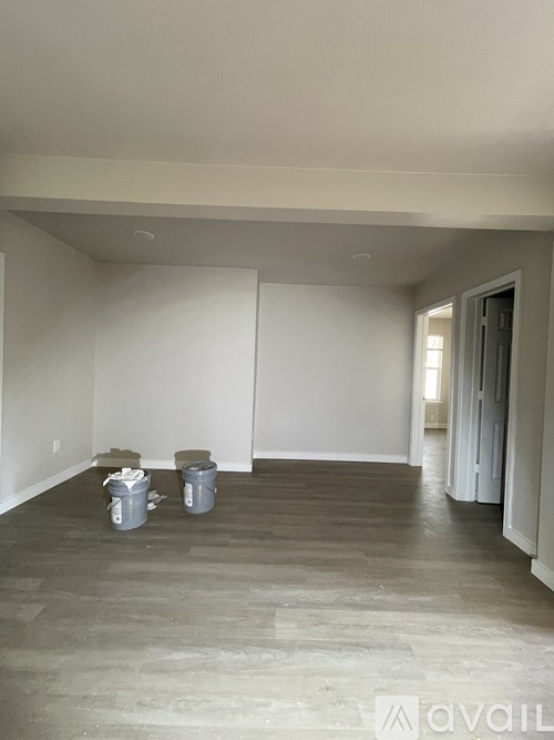 Two white buckets are on a wooden floor in a room with white walls.